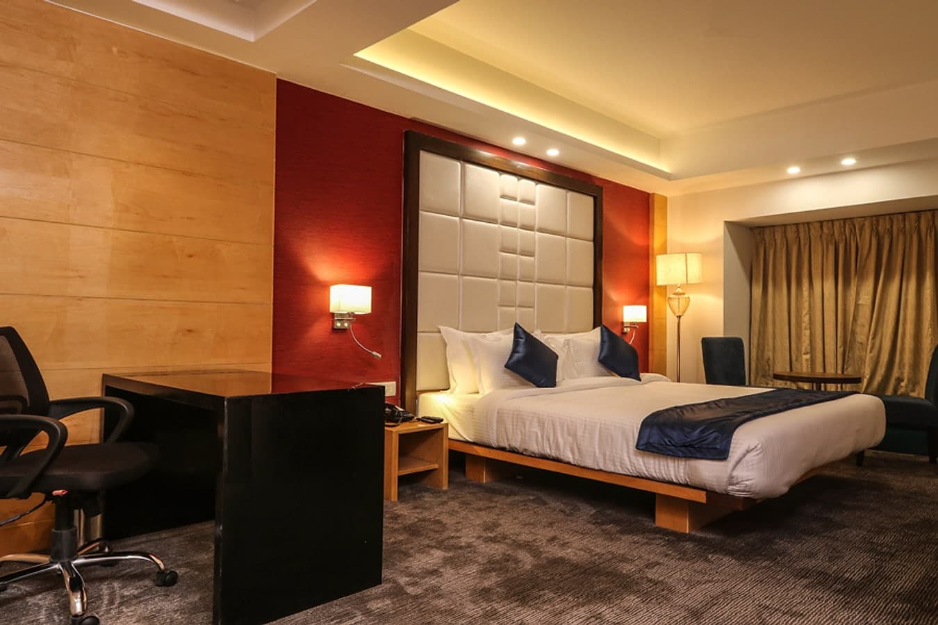 Executive room with a red accent wall, padded headboard and a dedicated work desk
