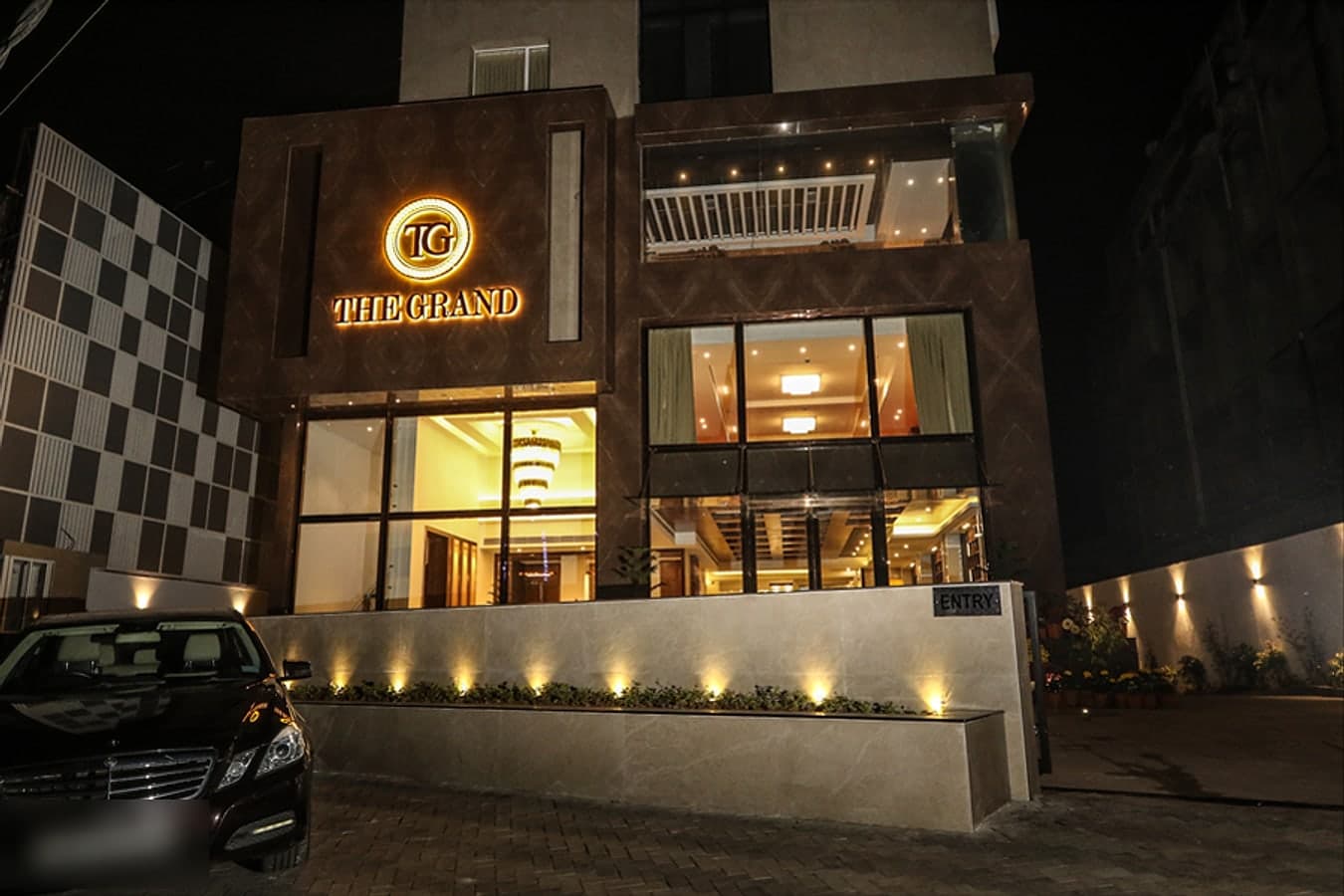The Grand hotel entrance at night with its glowing logo and chandelier-lit lobby