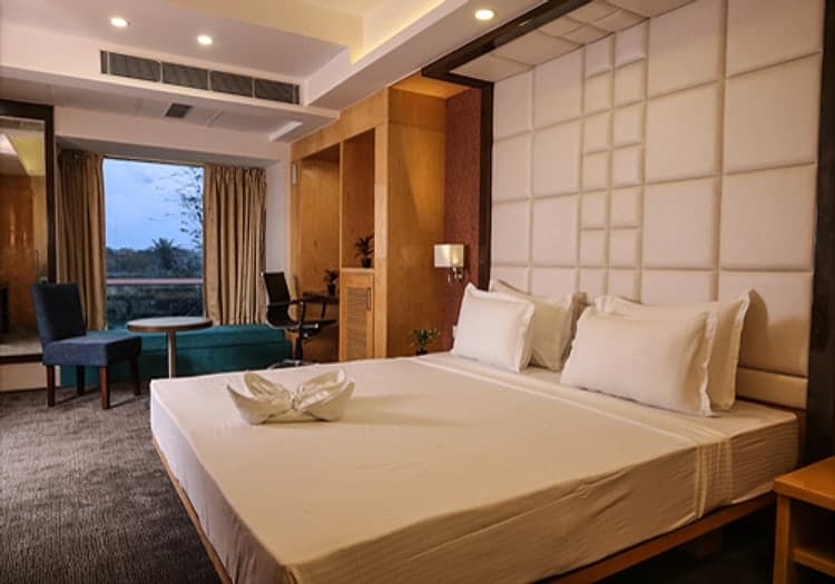 Suite bedroom with a king bed and open curtains framing palm trees at dusk