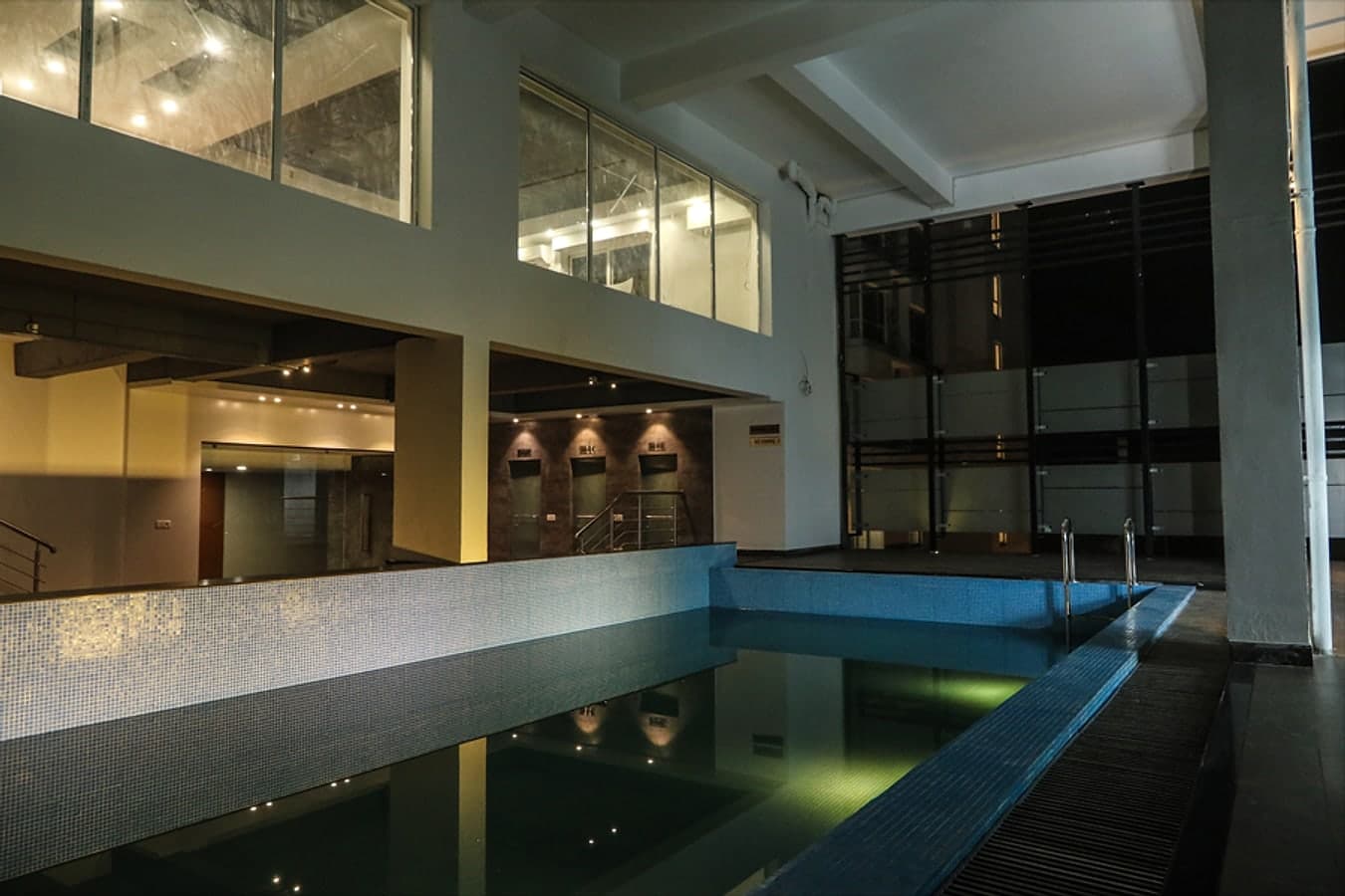 Swimming pool at night with underwater lights beneath a double-height space