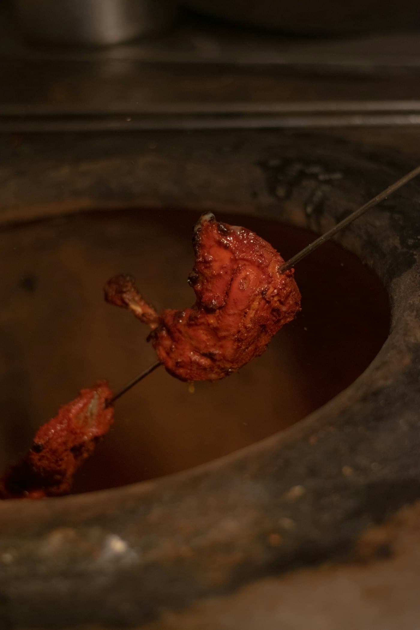 Tandoori chicken on a skewer cooking inside a clay tandoor