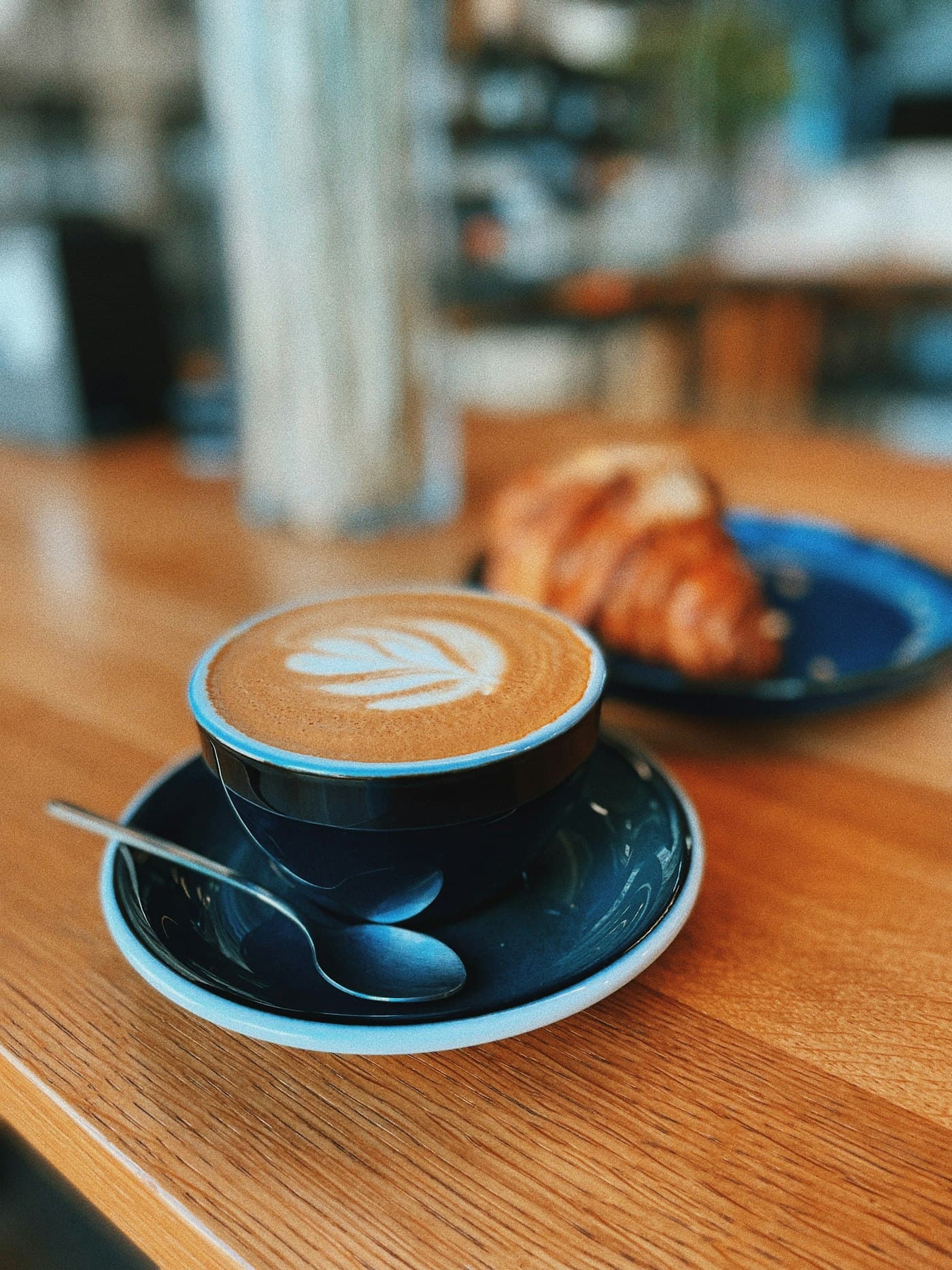 Cappuccino with latte art beside a croissant on a wooden café counter