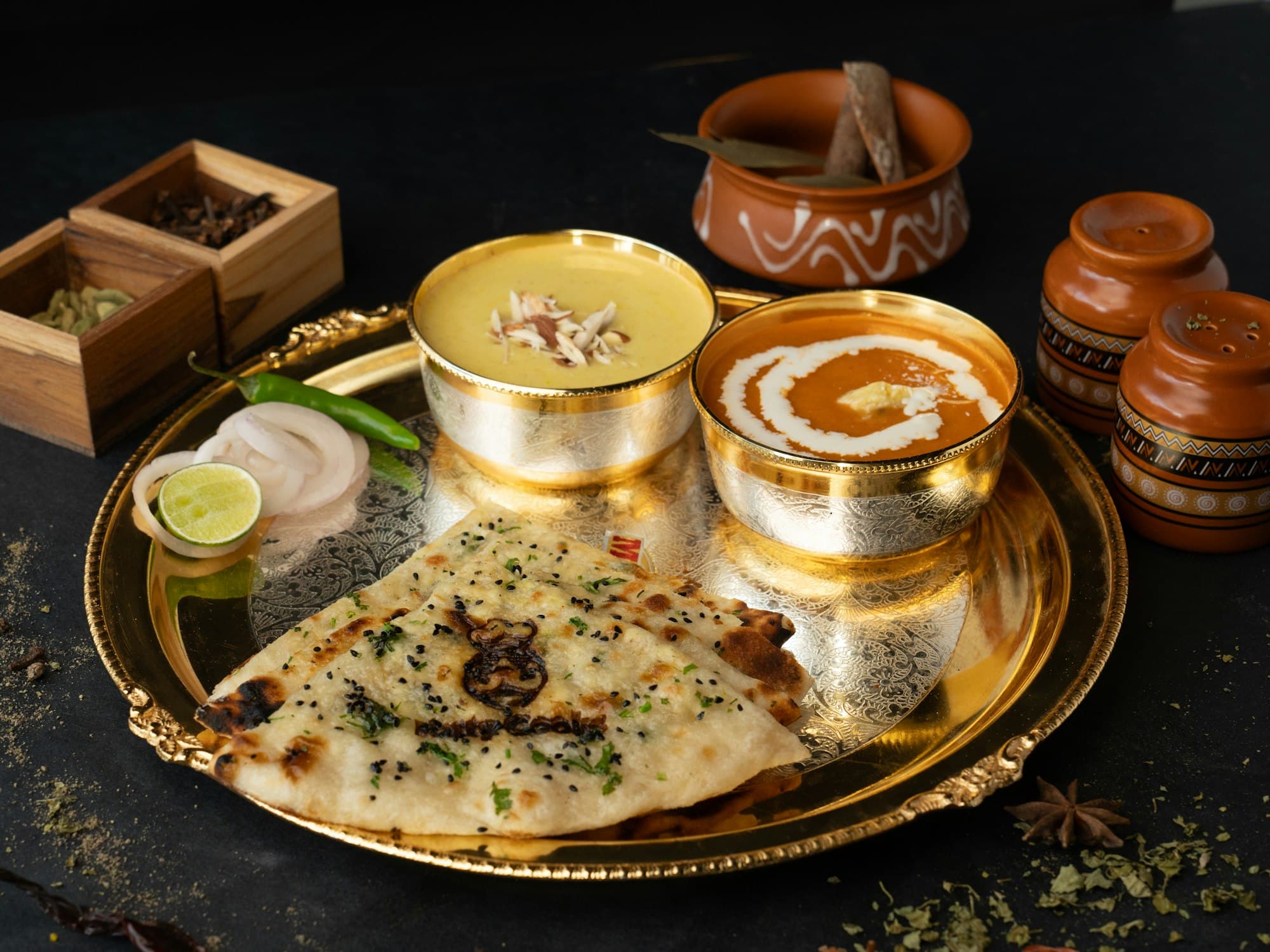 Dal makhani in a brass bowl with garlic naan on an ornate brass platter