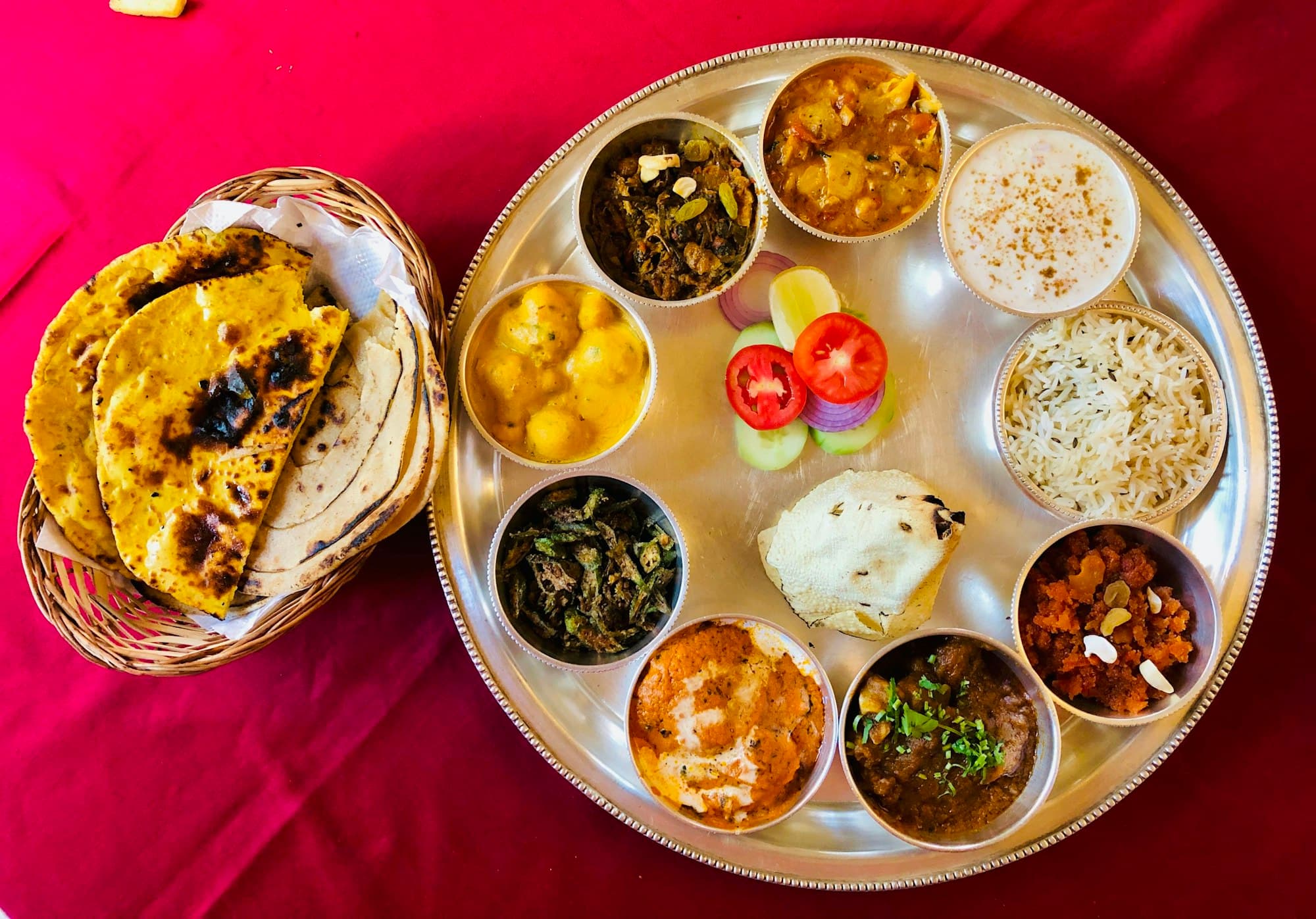 Overhead view of a vegetarian thali with ten small bowls and a basket of parathas