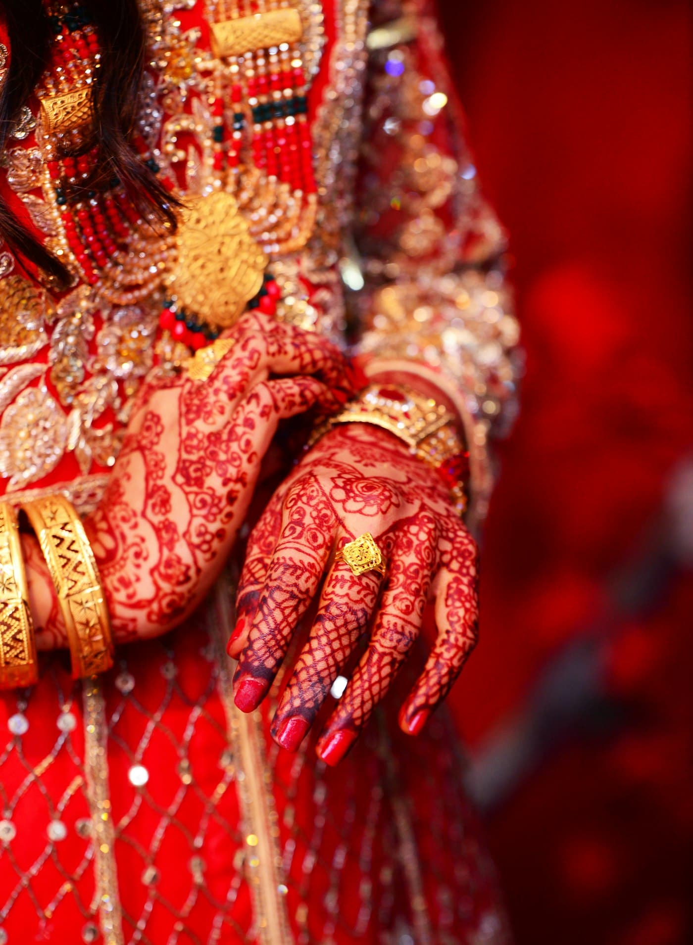A bride's hands decorated with mehendi, resting on a red sari